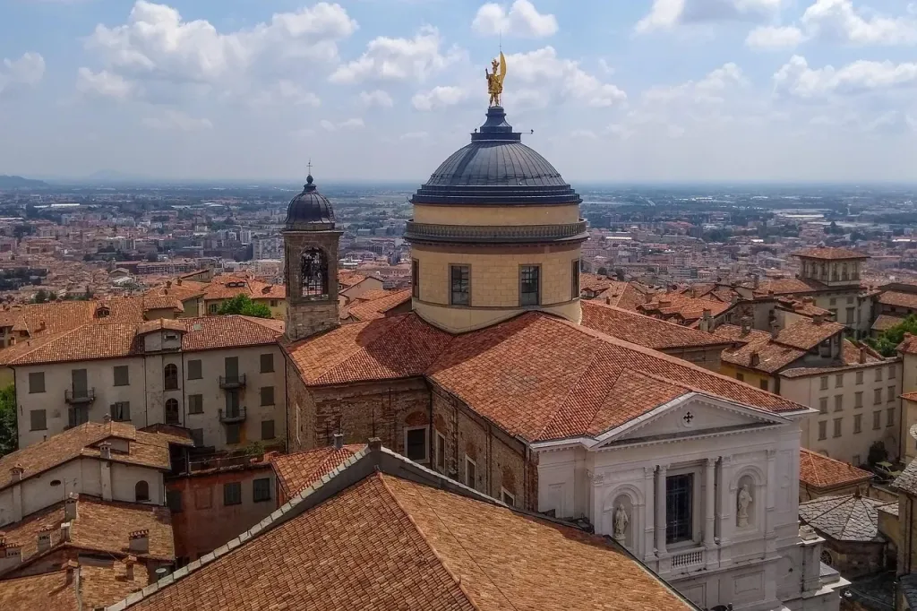 Panoramiczny widok na zabytkowe Bergamo Alta o zachodzie słońca, ukazujący średniowieczne mury i dachy miasta.